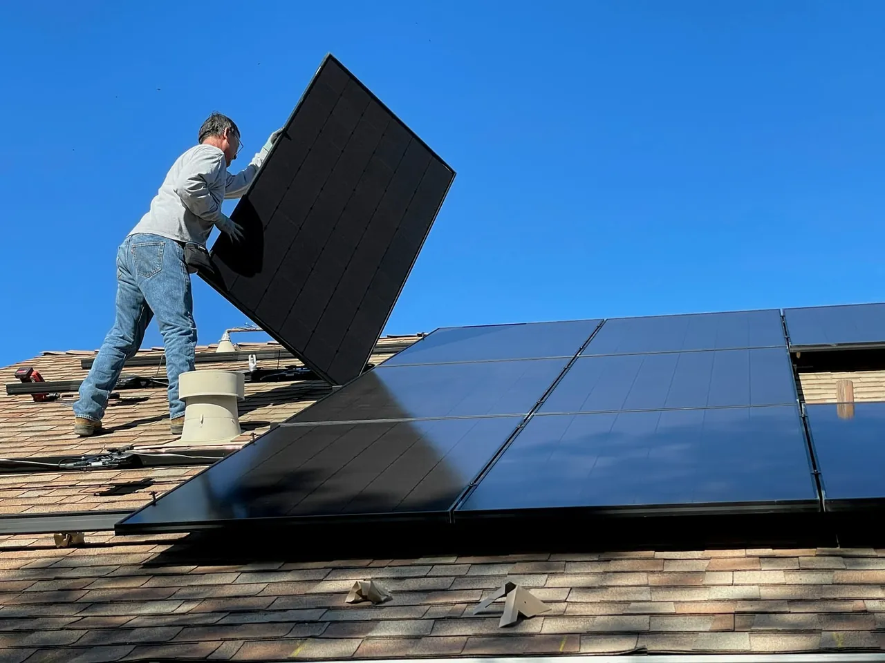 Solarteur setzt ein Solarmodul auf einem Schindeldach vor blauem Himmel ab
