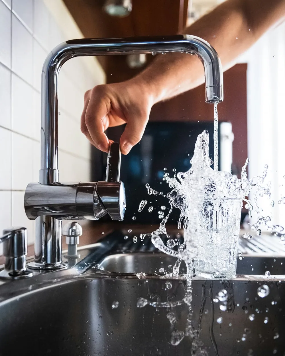 Glas unter einem laufenden Wasserhahn, den der Anlagenmechaniker in einer modernen Küche montiert hat